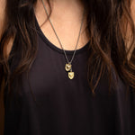 Woman wearing the Courageous Love Tags necklace featuring two 14k gold vermeil shield-and-heart pendants on a silver chain, shown against a black tank top.
