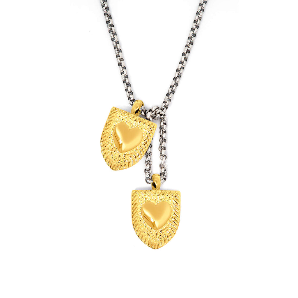 Close-up of two Courageous Love Tag pendants in 14k gold vermeil on a silver chain, featuring shield-shaped designs with raised heart centers, displayed against a white background.