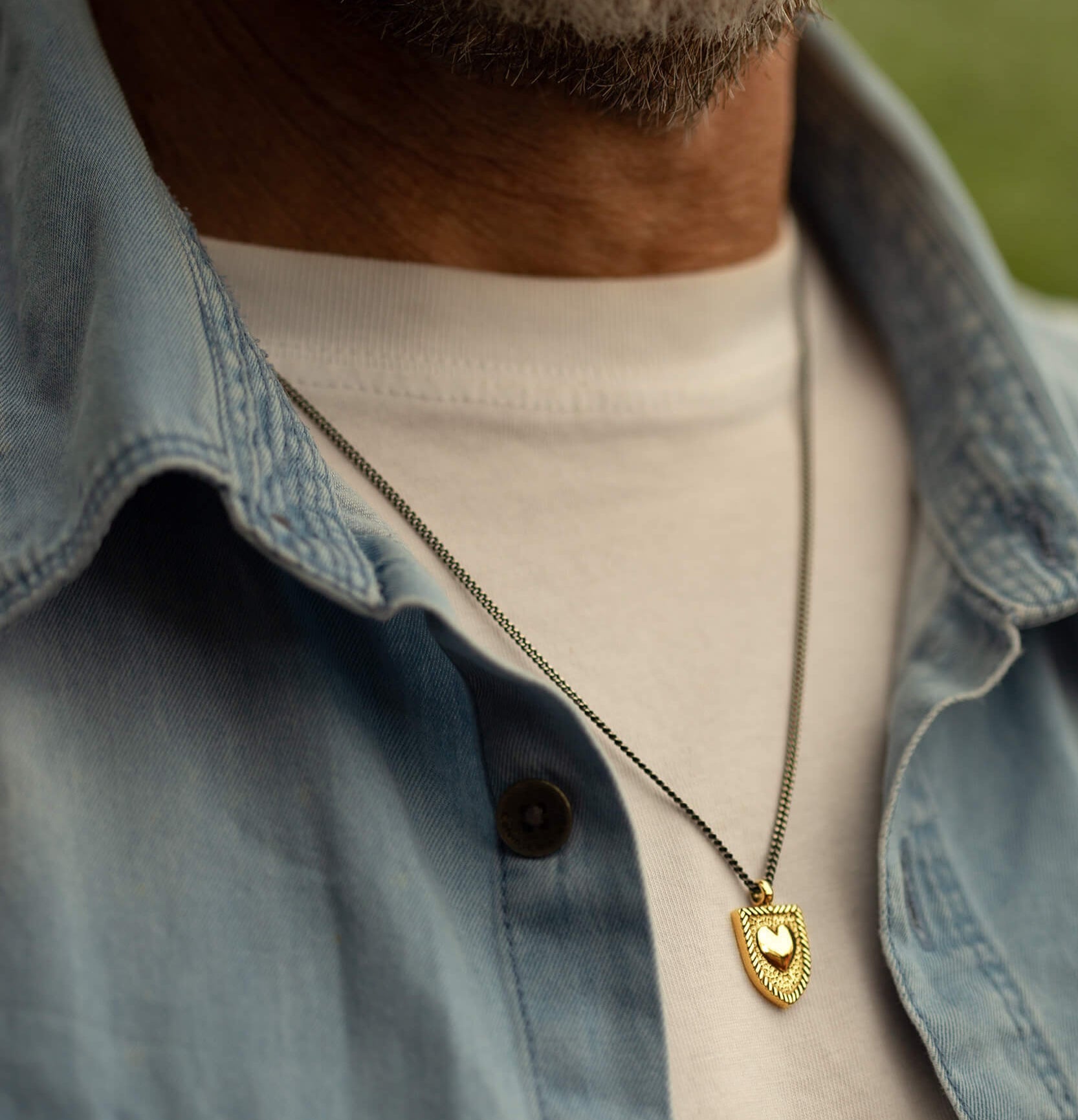 Man wearing the Courageous Love Necklace in 14k gold vermeil with shield pendant and heart center, symbolizing strength, resilience, and love.