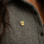 Courageous Love Pin in 14k gold vermeil with shield and heart design, worn on a grey knit sweater, symbolizing strength, resilience, and love.
