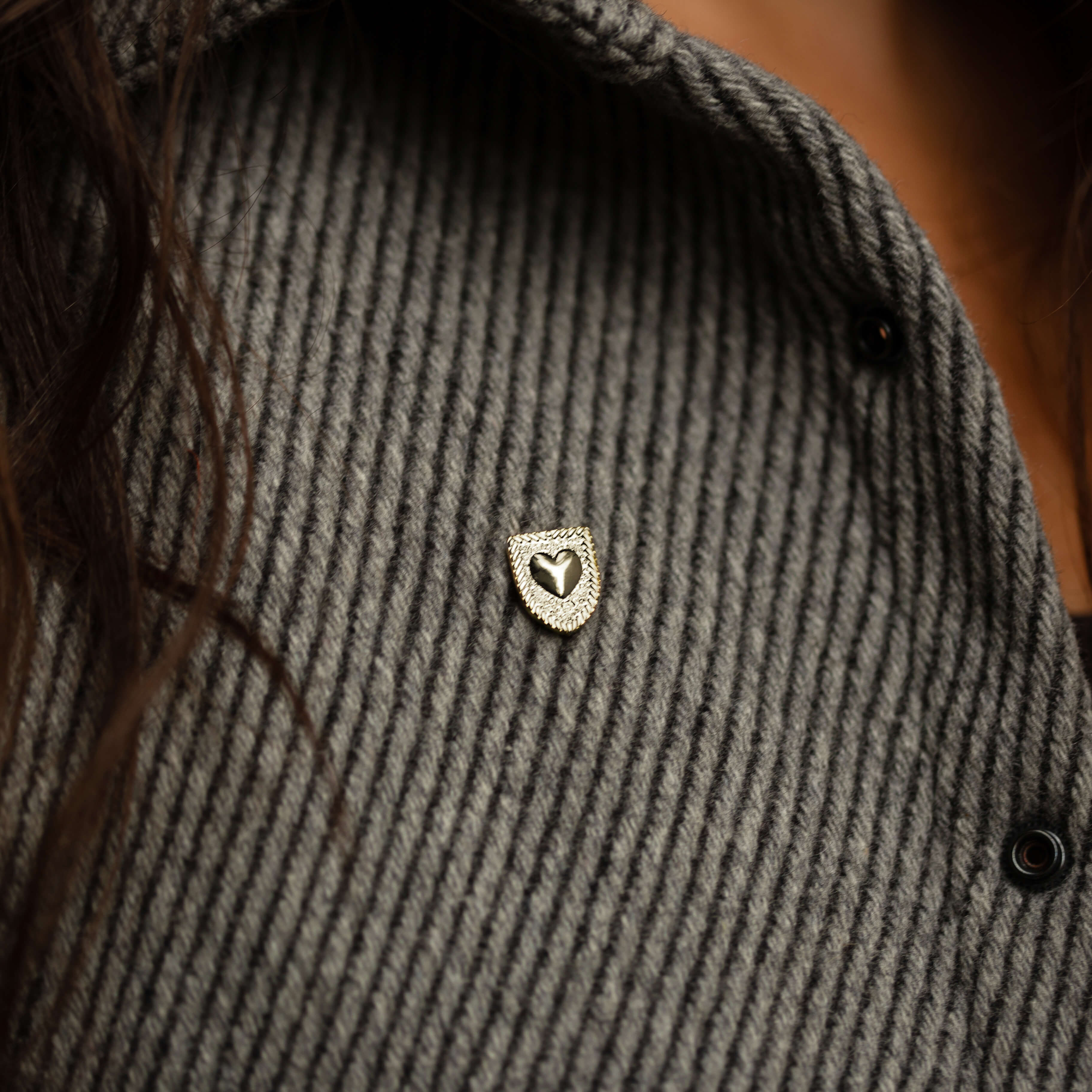 Courageous Love Pin in sterling silver with shield and heart design, worn on a grey knit sweater, symbolizing strength, resilience, and love.