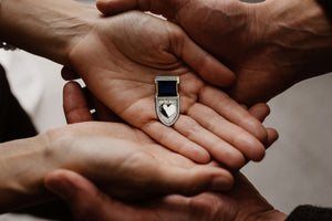 Hands gently holding a sterling silver Love Medal with a heart at the center, symbolizing love, courage, and recognition.