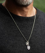 Man wearing the Courageous Love Tags necklace in sterling silver with two shield-shaped pendants featuring heart centers, symbolizing love and connection